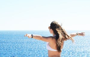 A woman in a bikini enjoying a sunny day by the sea with open arms in Sharm El Sheikh, Egypt.