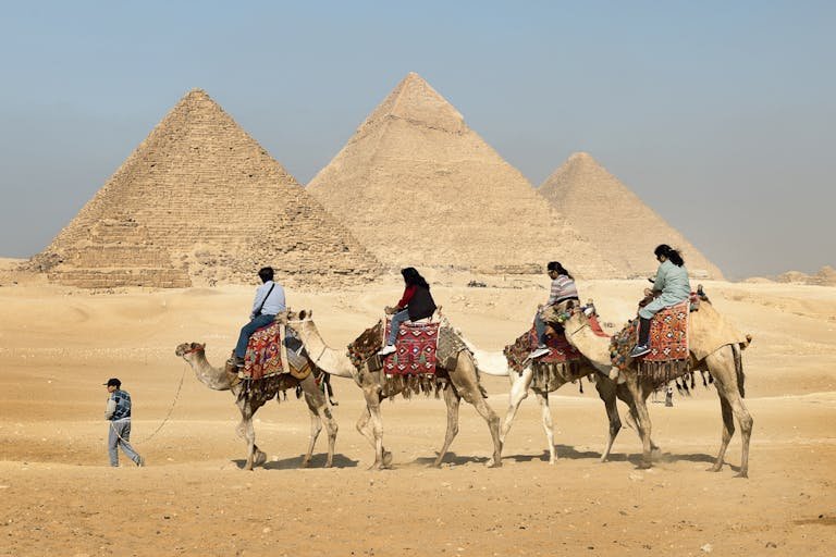 Tourists riding camels near the Great Pyramids of Giza, Egypt under clear skies.
